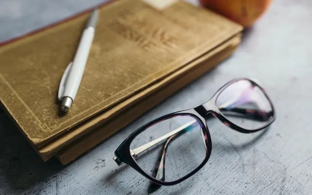 Reading materials on a desk with glasses a pen and an apple nearby