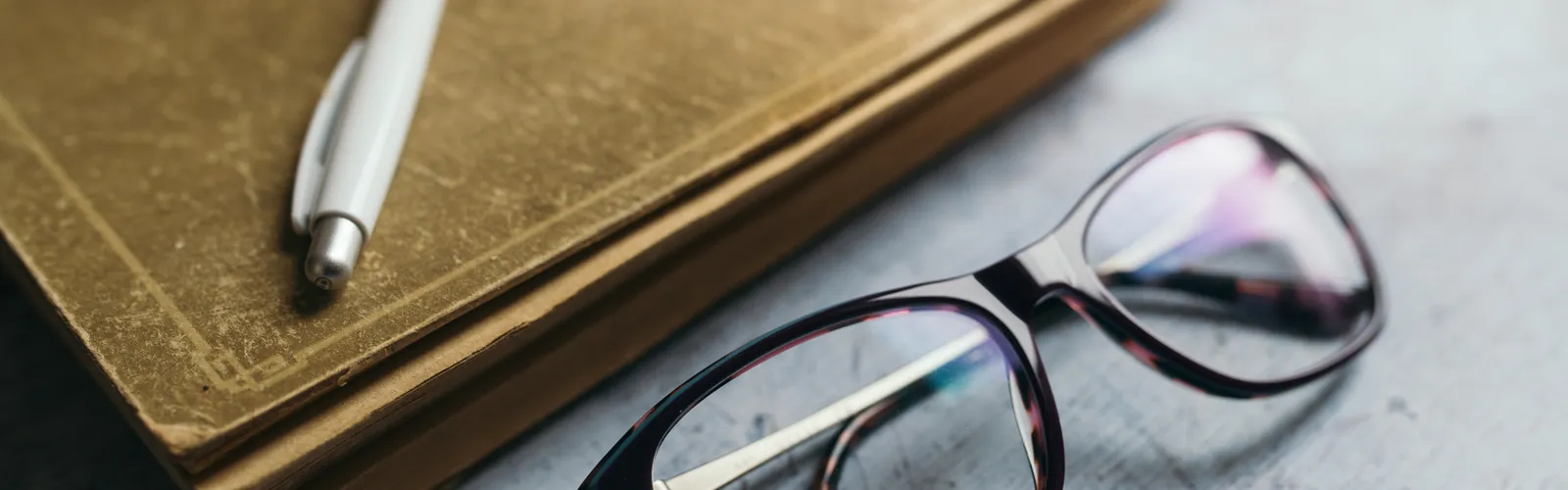 Reading materials on a desk with glasses a pen and an apple nearby